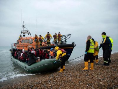 Migrants are helped ashore from a RNLI (Royal National Lifeboat Institution) lifeboat at a beach in Dungeness, on the south-east coast of England, on November 24, 2021, after being rescued while crossing the English Channel. The past three years have seen a significant rise in attempted Channel crossings by migrants, despite warnings of the dangers in the busy shipping lane between northern France and southern England, which is subject to strong currents and low temperatures. (Photo by Ben STANSALL / AFP)